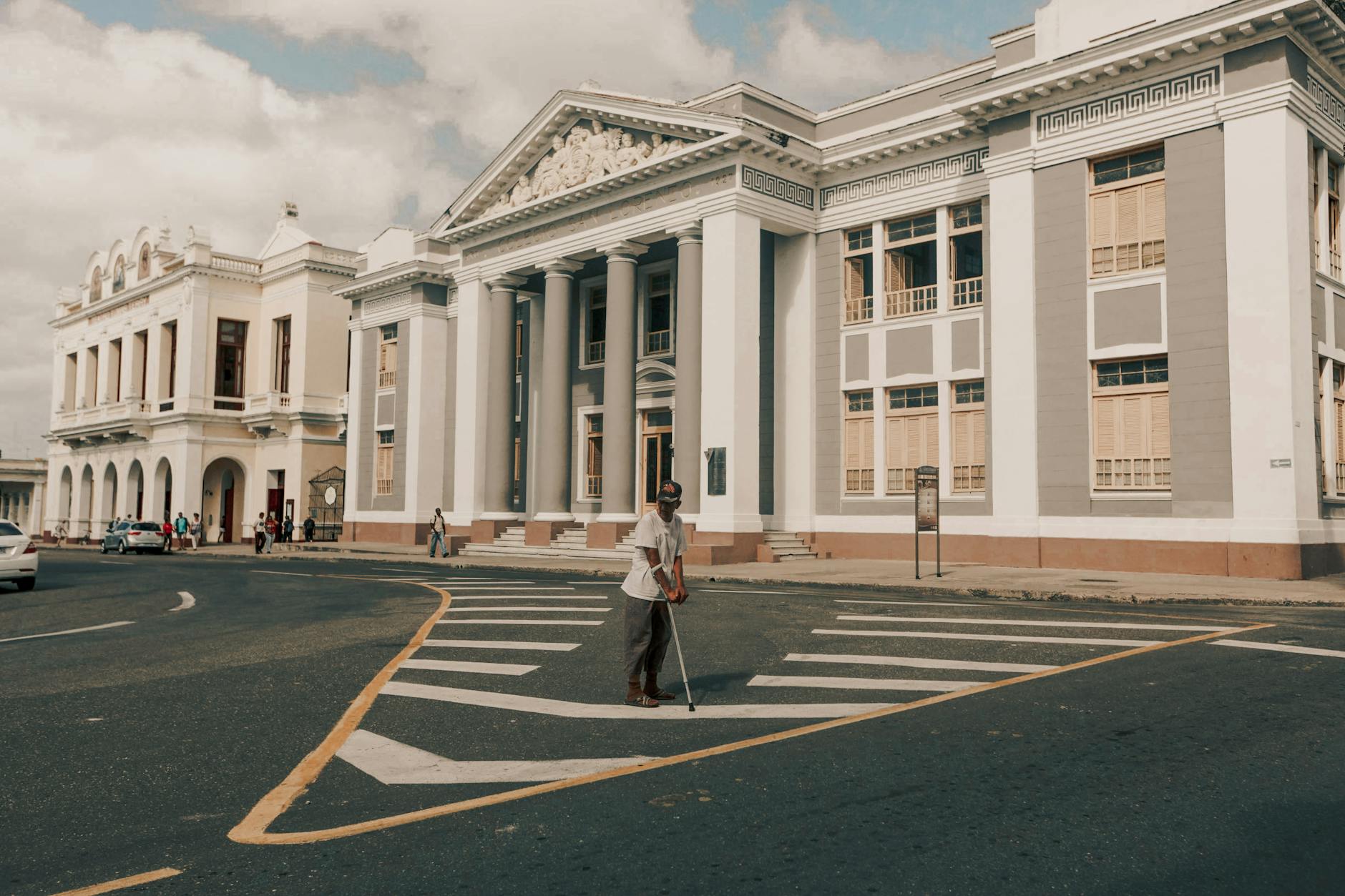 Starszy mężczyzna z laską przechodzi przez pustą ulicę przy dużym budynku