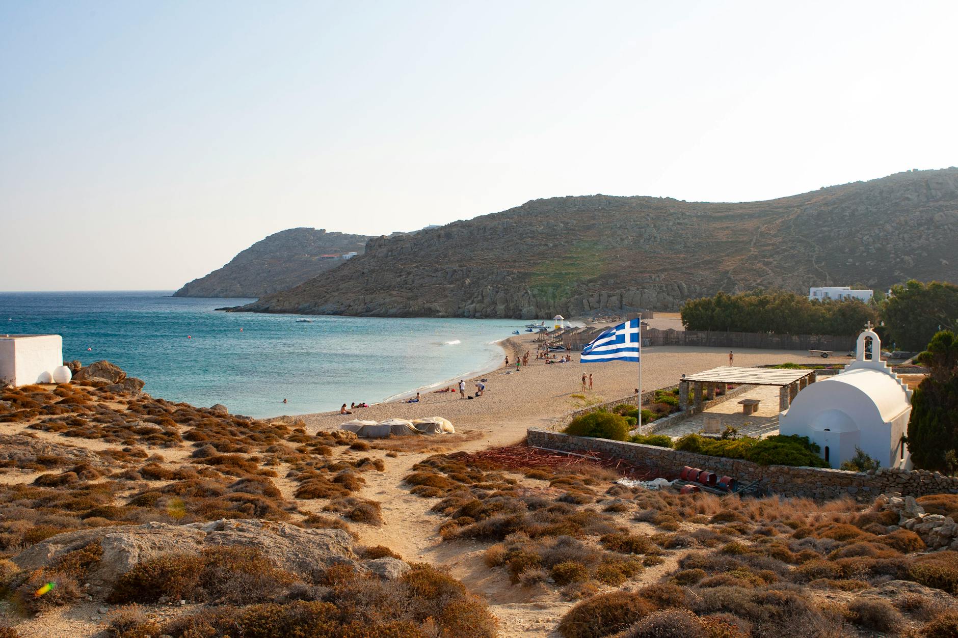 Plaża na Mykonos z grecką flagą i białym kościołem nad morzem